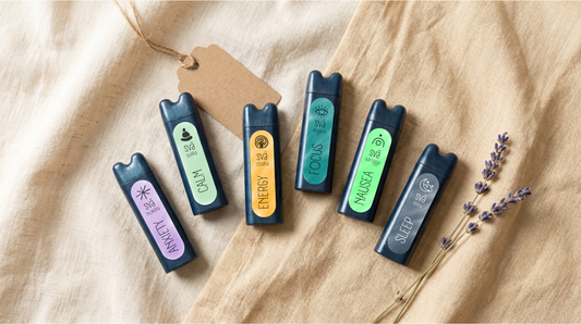 Entire collection of Svaroma aromatherapy inhalers lying on a linen surface along with a sprig of lavender. Products depict Anxiety, Calm, Energy, Focus, Nausea, Sleep aromatherapy inhalers